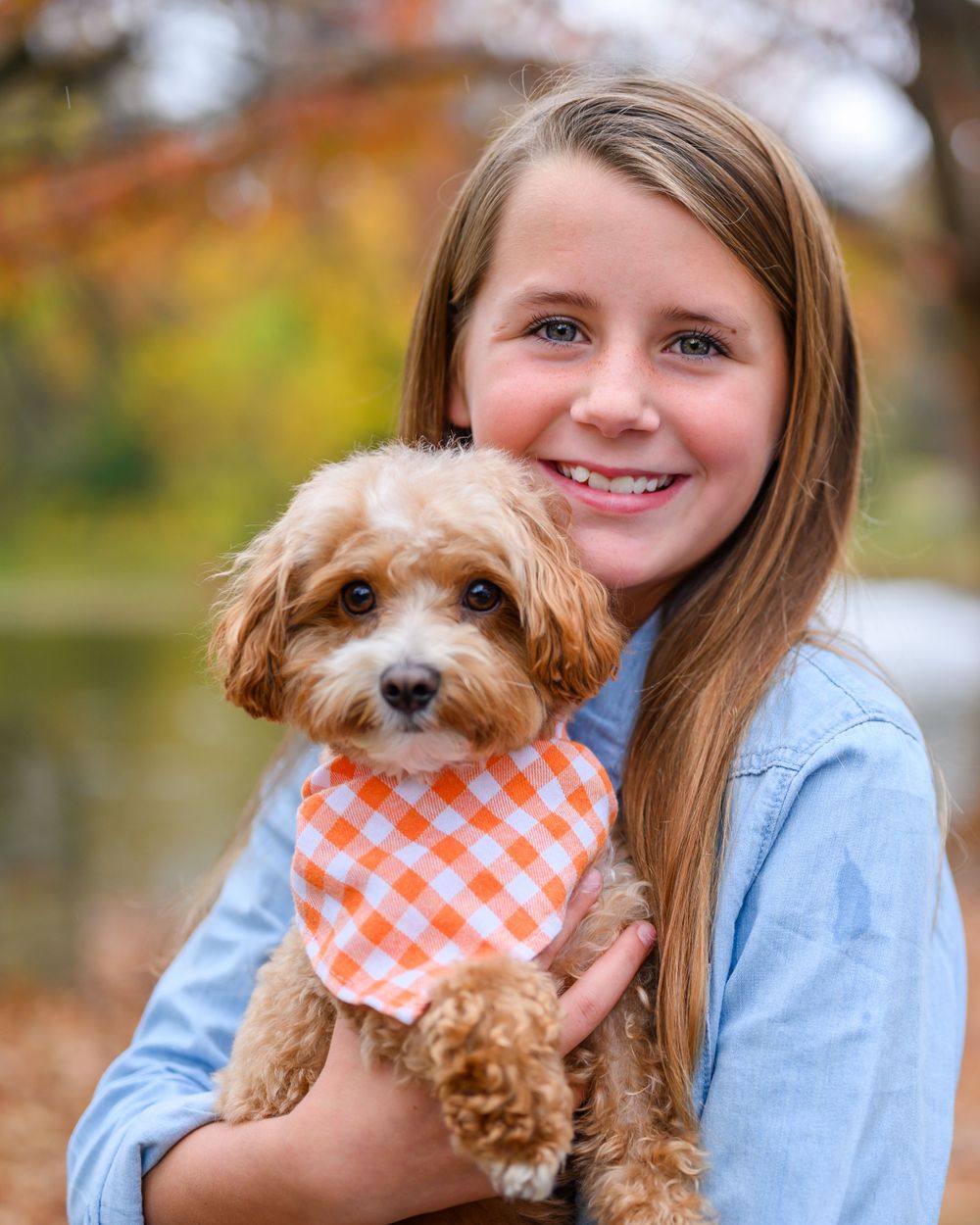 A cheerful scene with a young person holding a small brown dog wearing an orange checkered bandana.