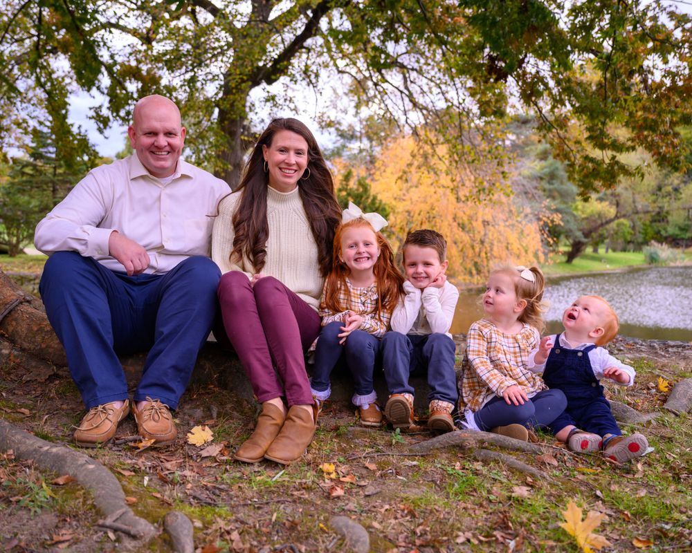 Family of six sitting together on log during autumn photoshoot.