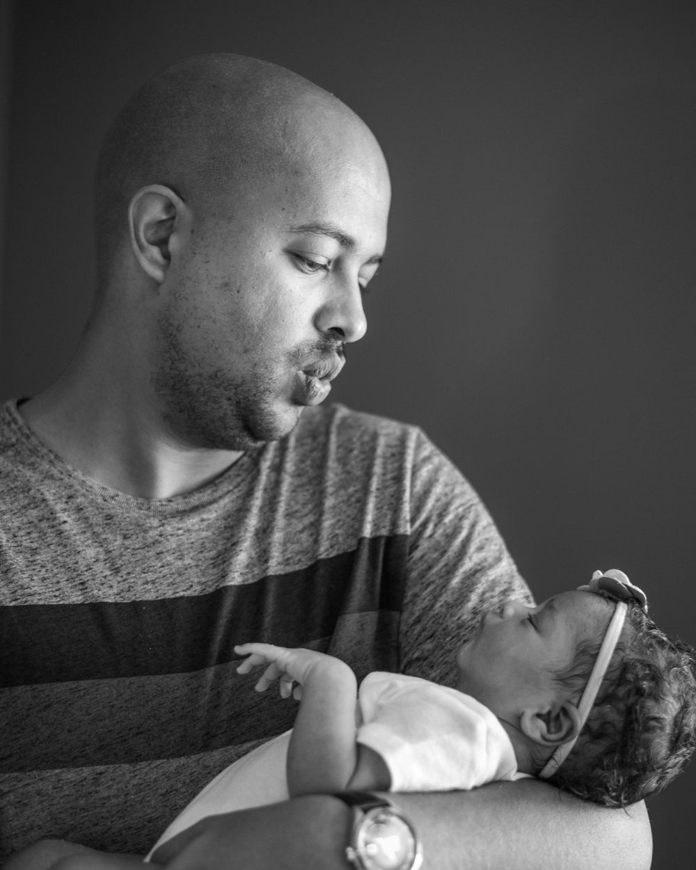 Black and white portrait capturing intimate parenting moment against dark background.