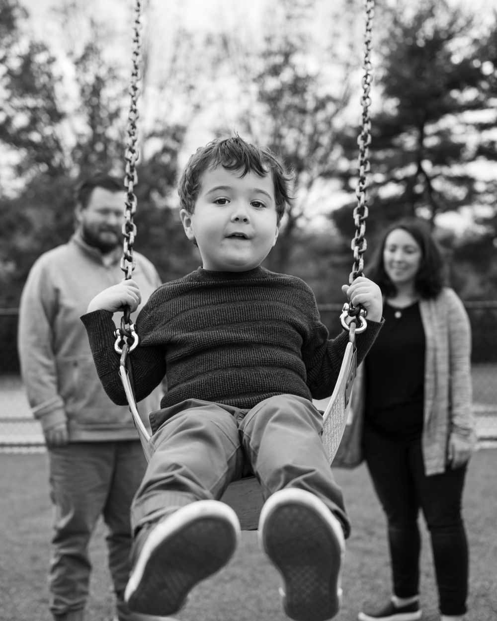 Child swinging at playground with adults watching in background.
