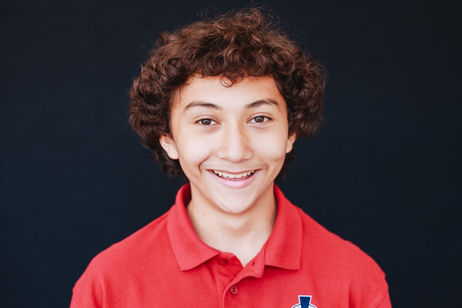 Portrait of student in red polo with curly hair and bright smile.