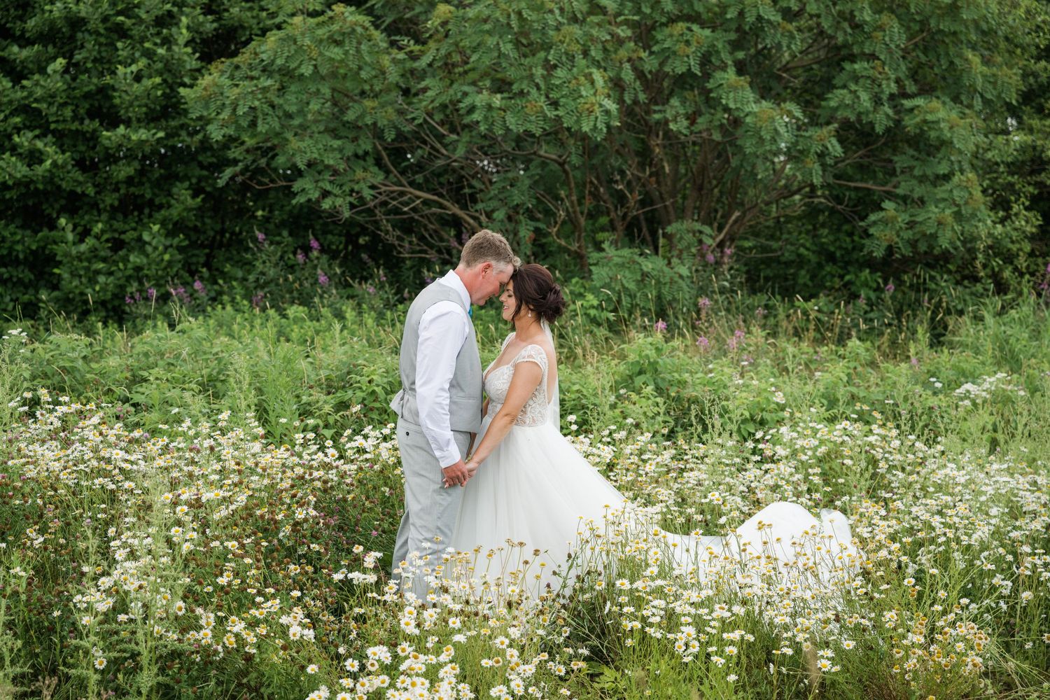 Romantic wedding portrait in a field of white wildflowers on a summer day.