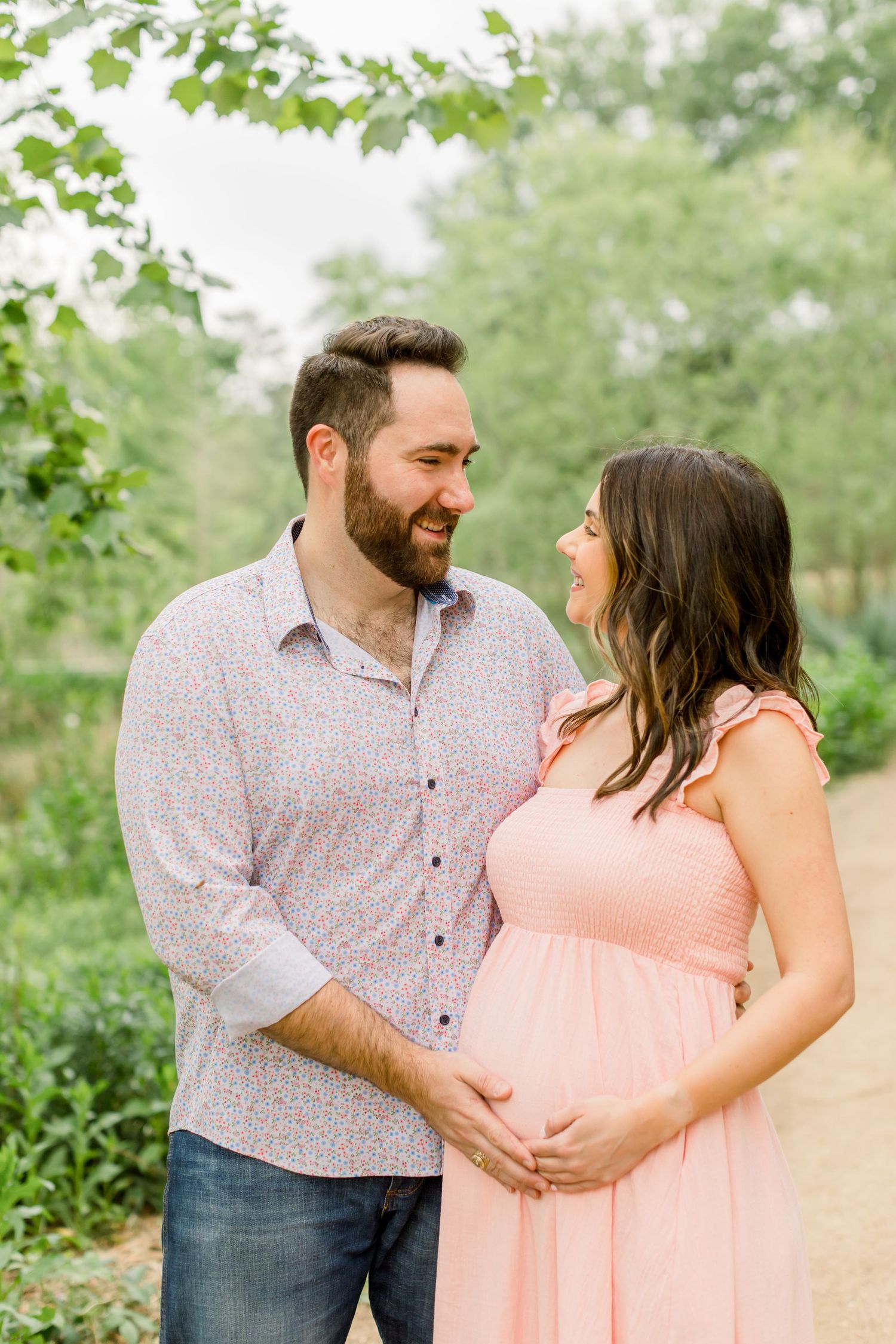 A couple shares a joyful moment on a nature path while expecting a baby.