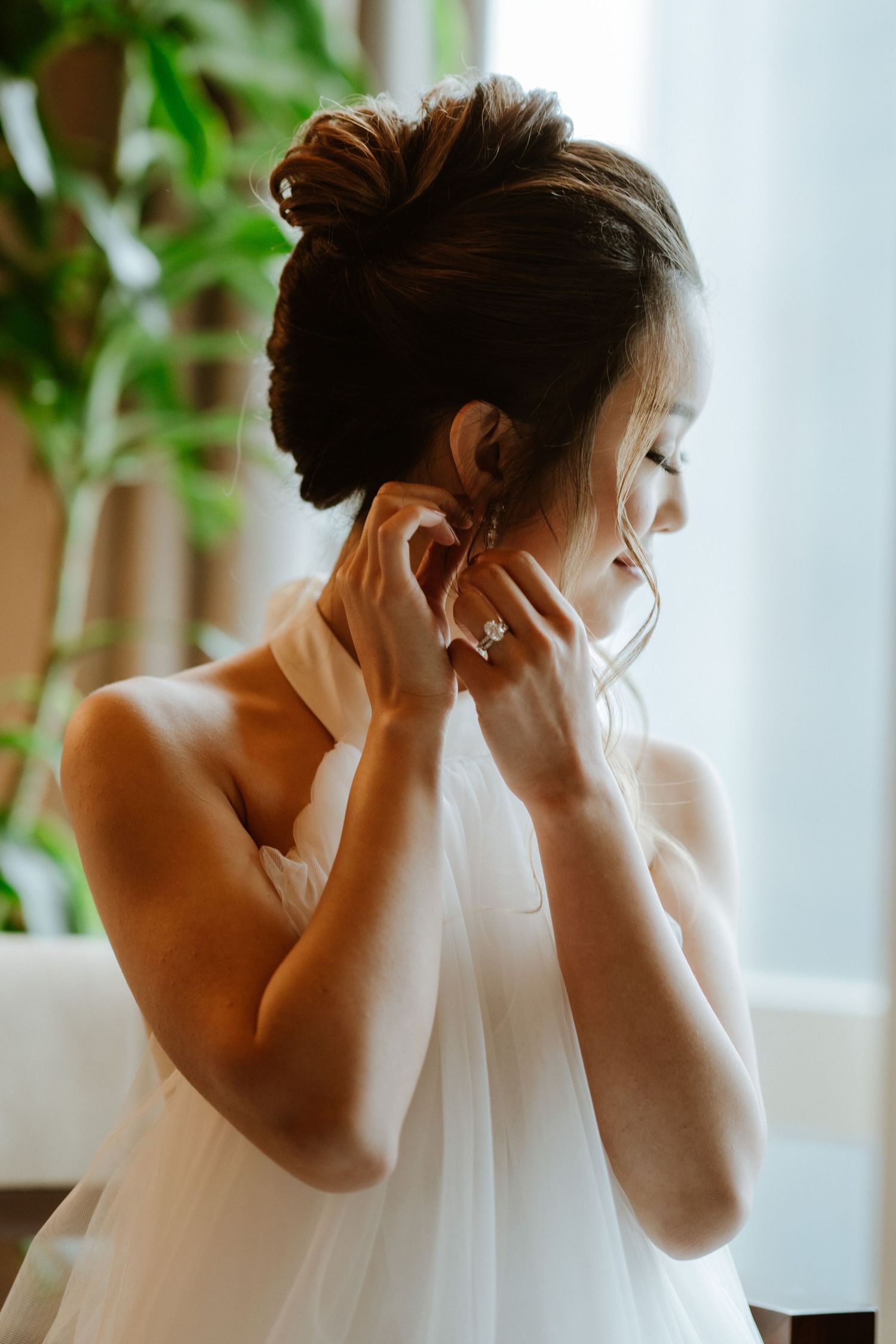 Elegant bridal preparation moments captured through sheer white curtains with green plants.