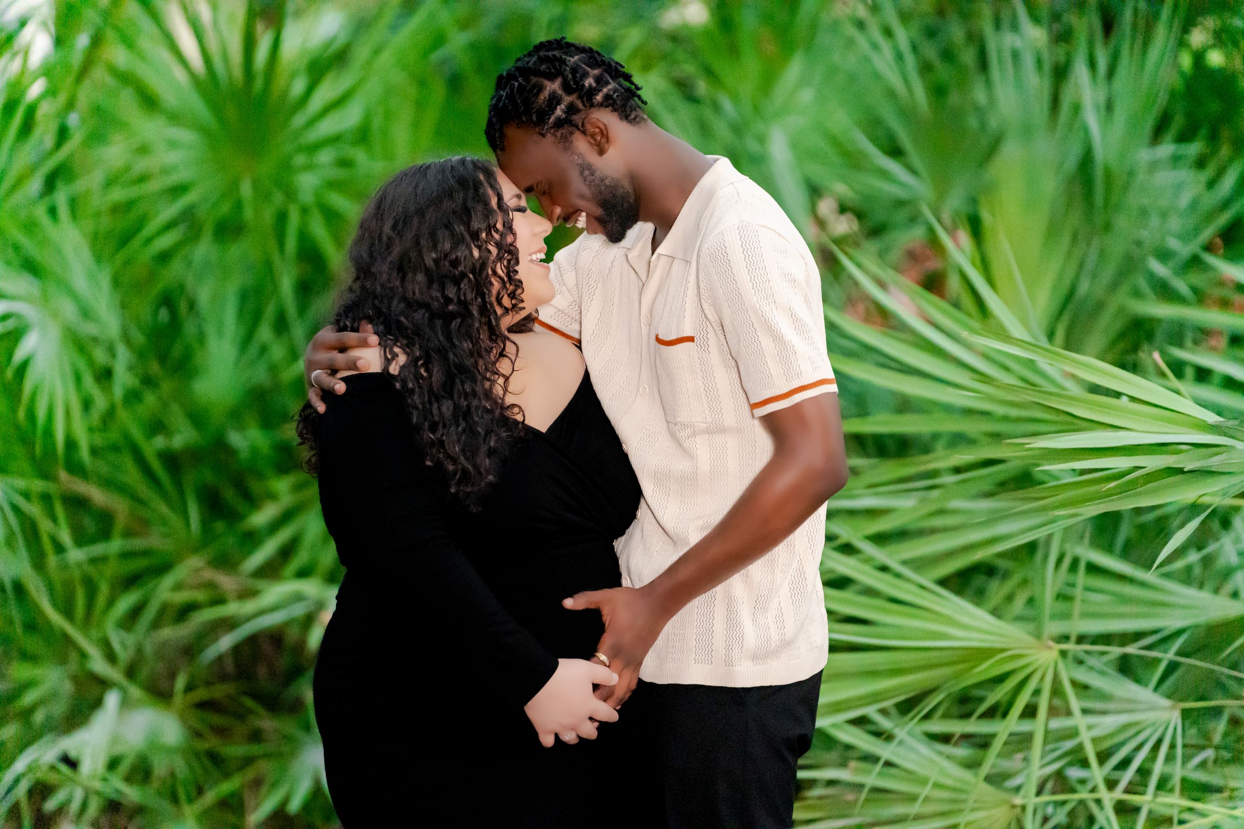A couple shares an intimate moment while holding hands against a lush tropical palm background.