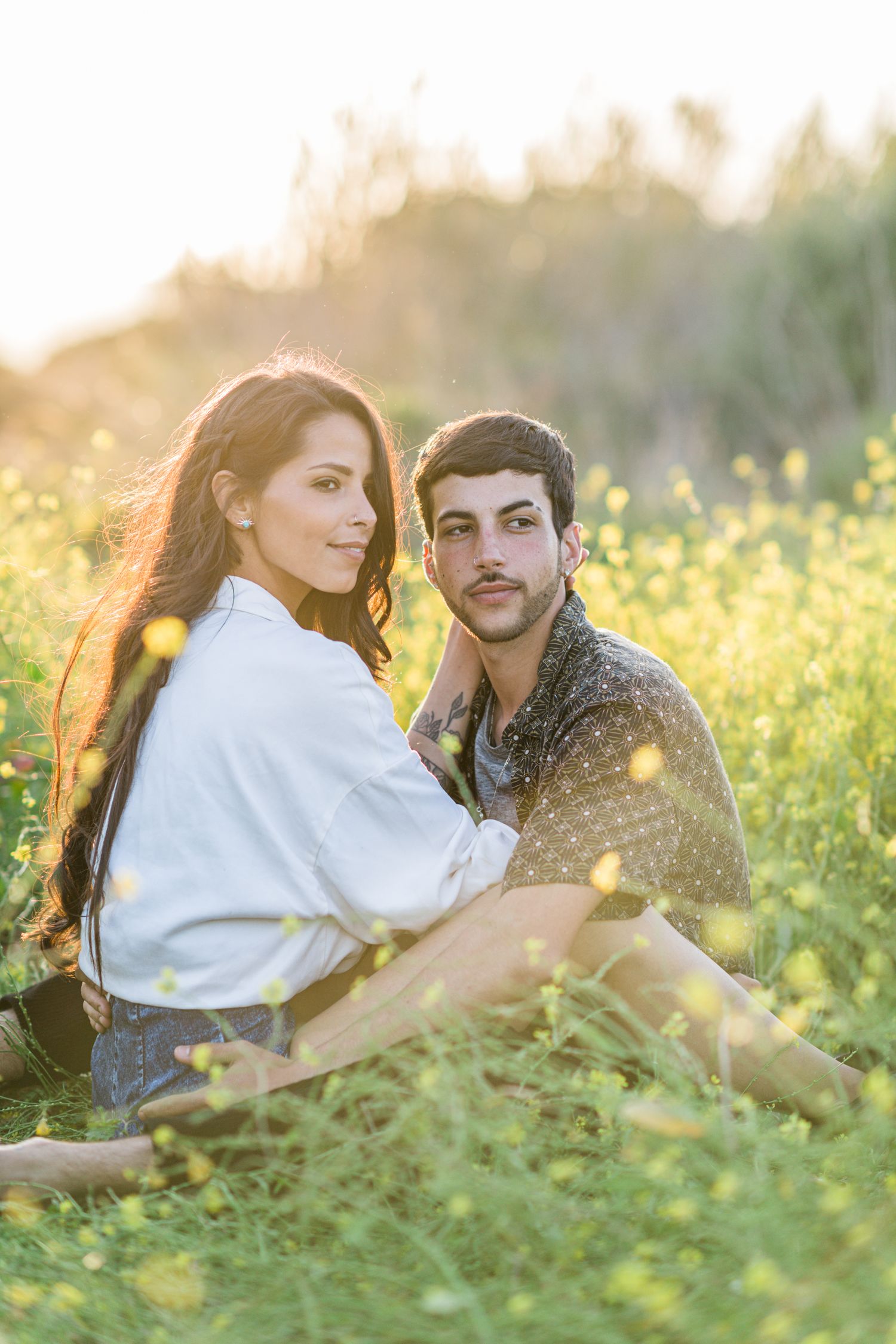 A young couple embrace and smiles in a field of yellow flowers