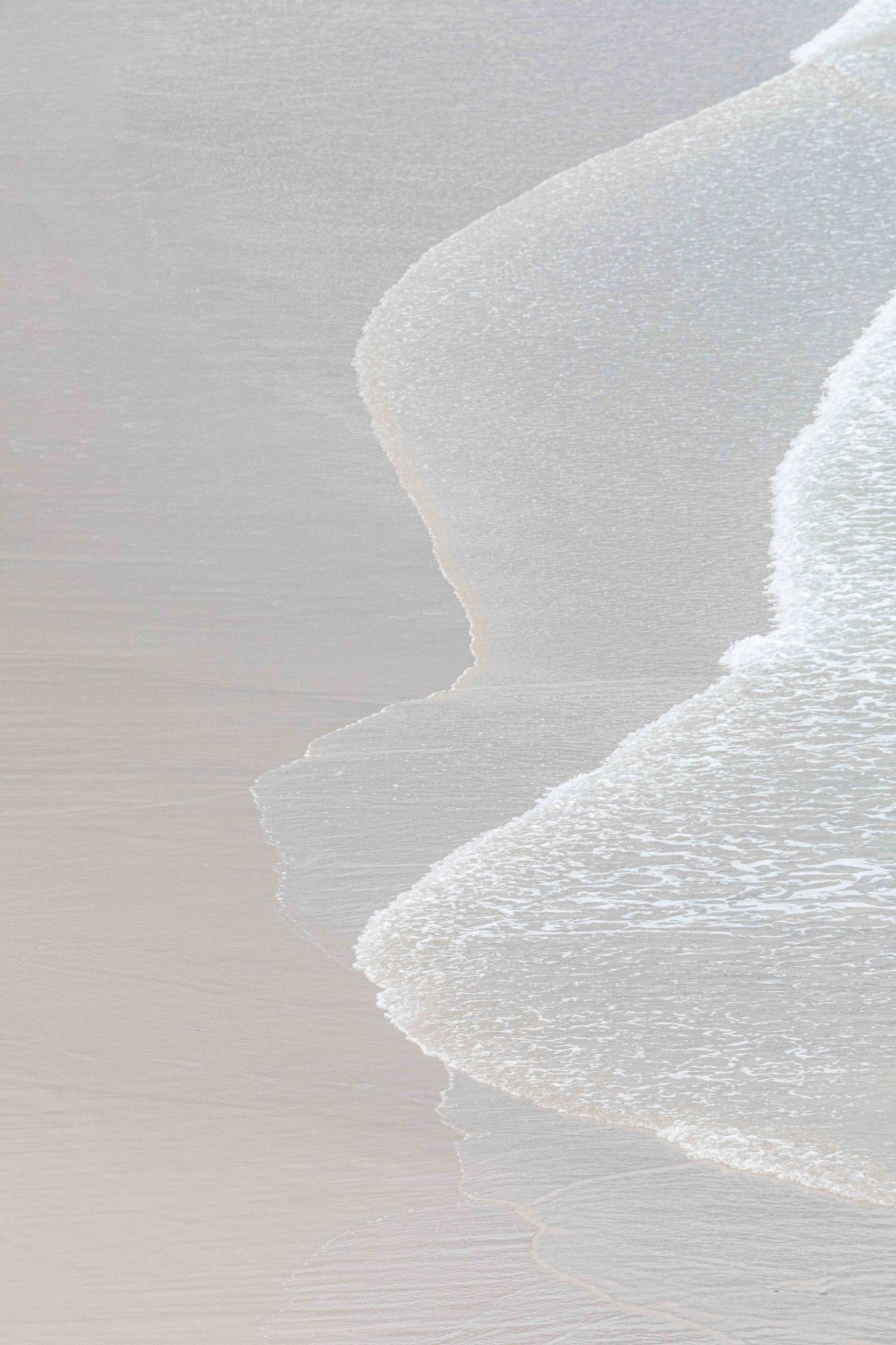 Gentle ocean waves create smooth curves on pristine sandy beach.