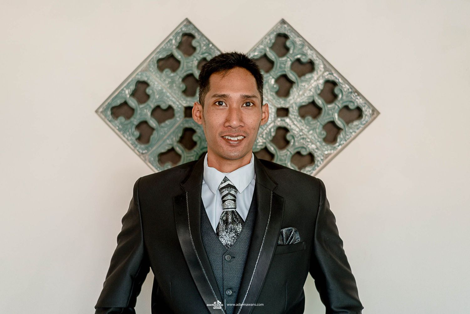 Formal portrait against geometric wall art featuring a black tuxedo with silver accents.