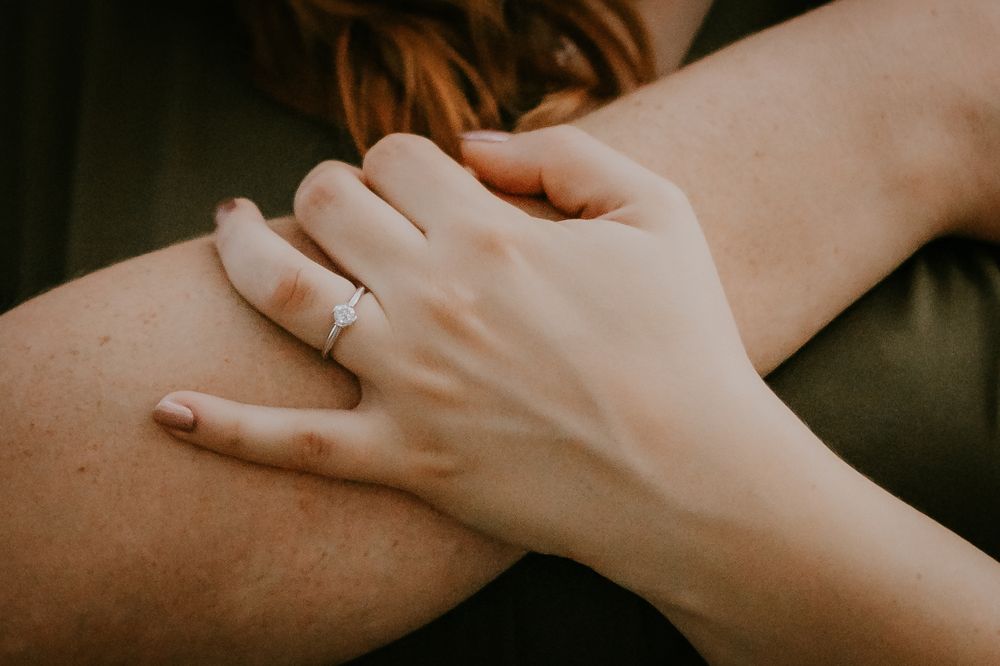 Close up of hands with engagement ring resting on leg in intimate pose.