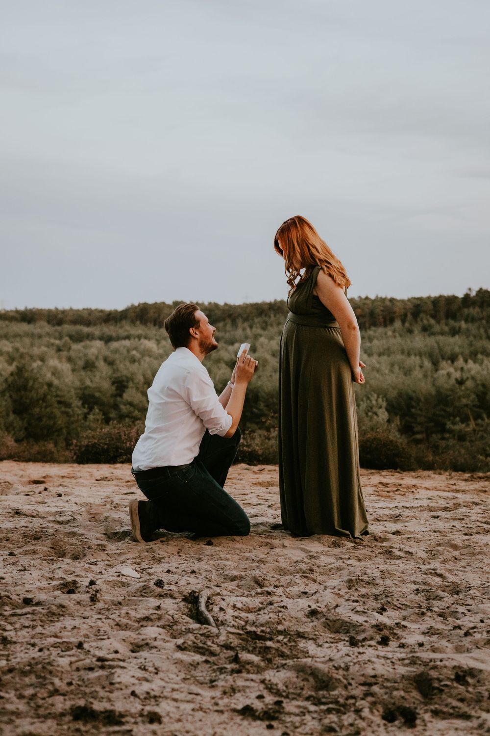 Romantic proposal scene on desert landscape during sunset.