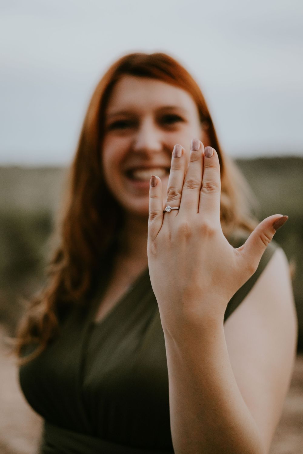 Woman showing off engagement ring with joyful expression in natural setting.