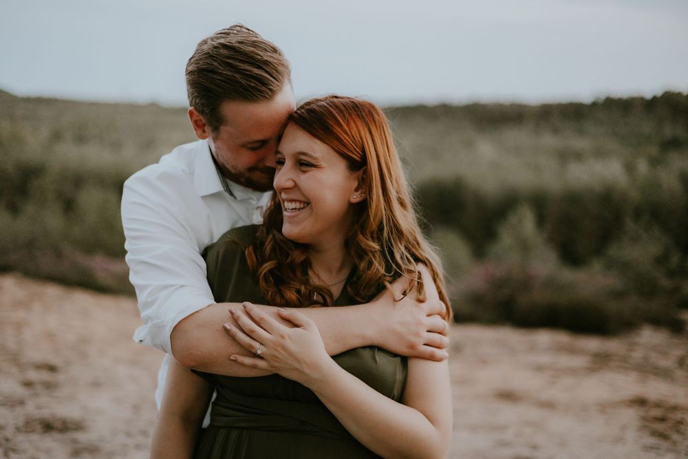 An intimate couple embraces and laughs together during an outdoor photo session at sunset.