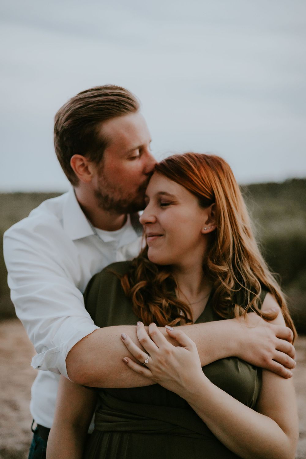 A loving couple embraces during an outdoor portrait session, with soft natural lighting and scenic backdrop.