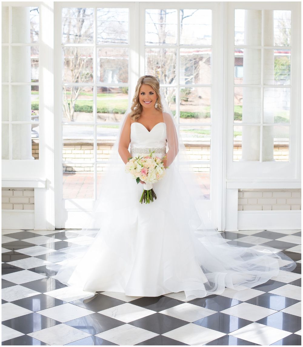 Bridal portrait on checkered floor with large windows and white bouquet.