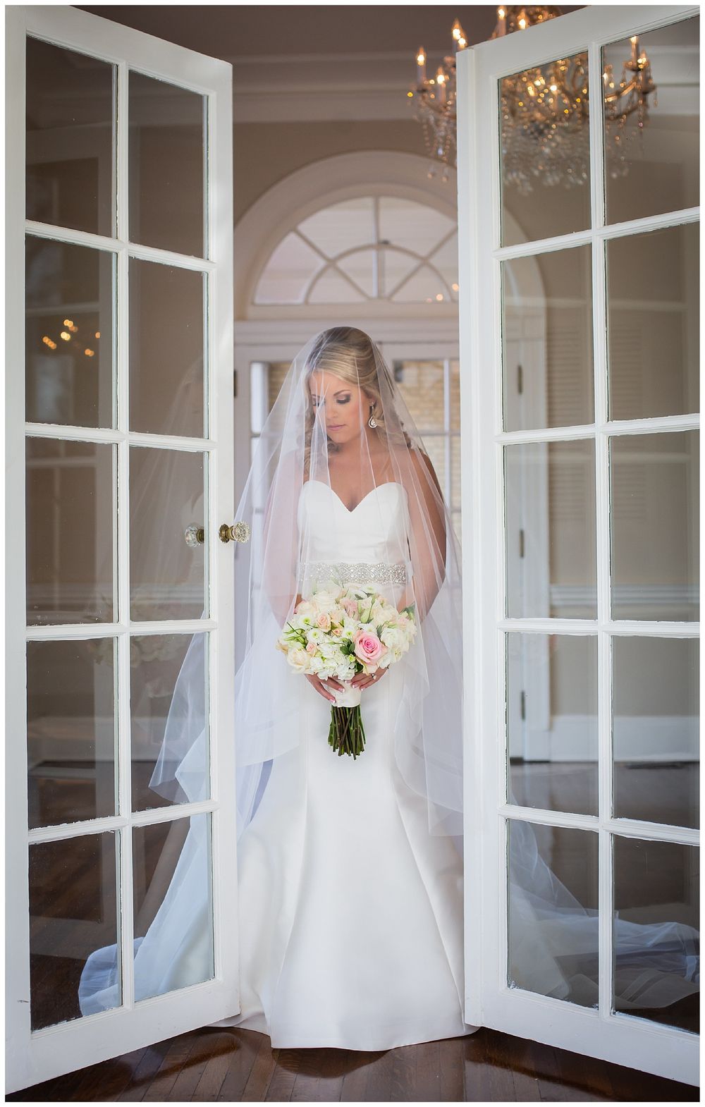 Romantic bridal portraits framed by French doors and chandelier in elegant indoor setting.