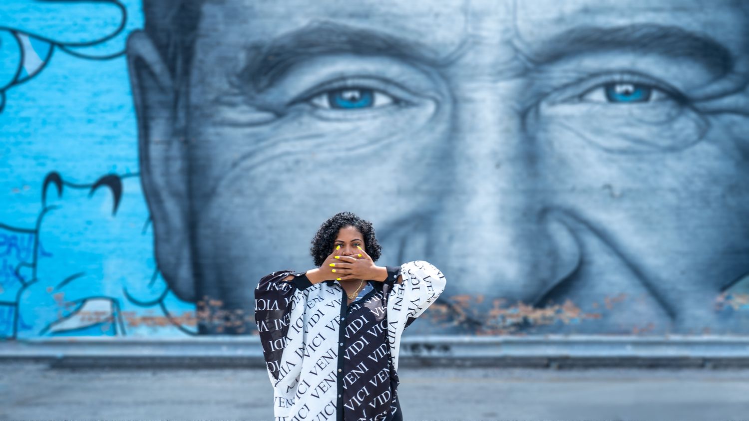 Person posing in front of large blue wall mural featuring close-up portrait.