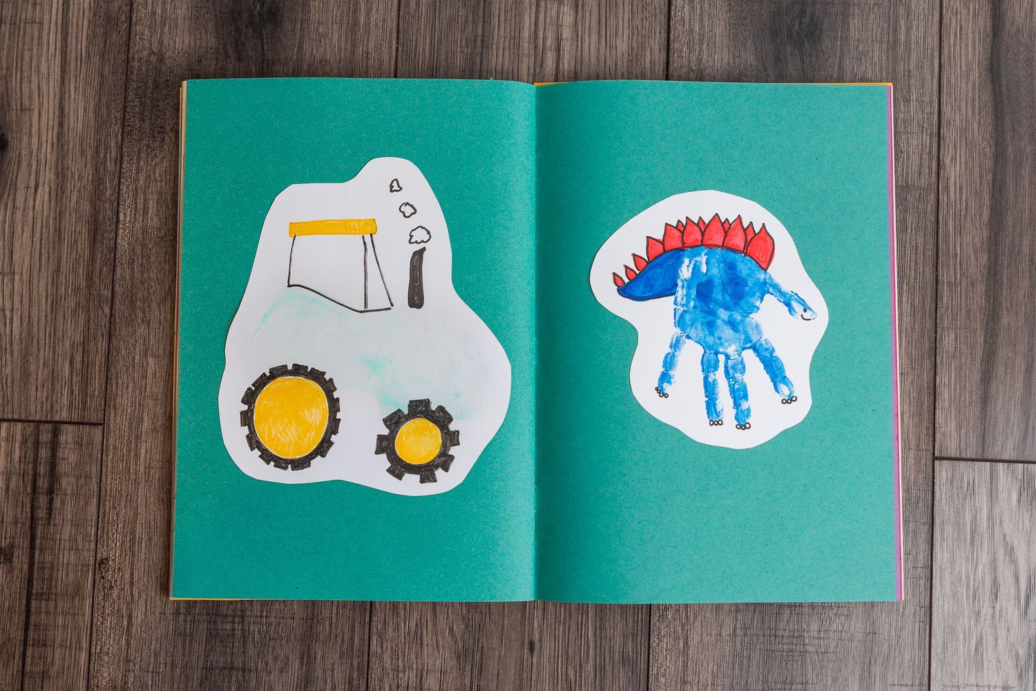 Children's artwork showing drawings of a tractor and handprint in a green notebook.