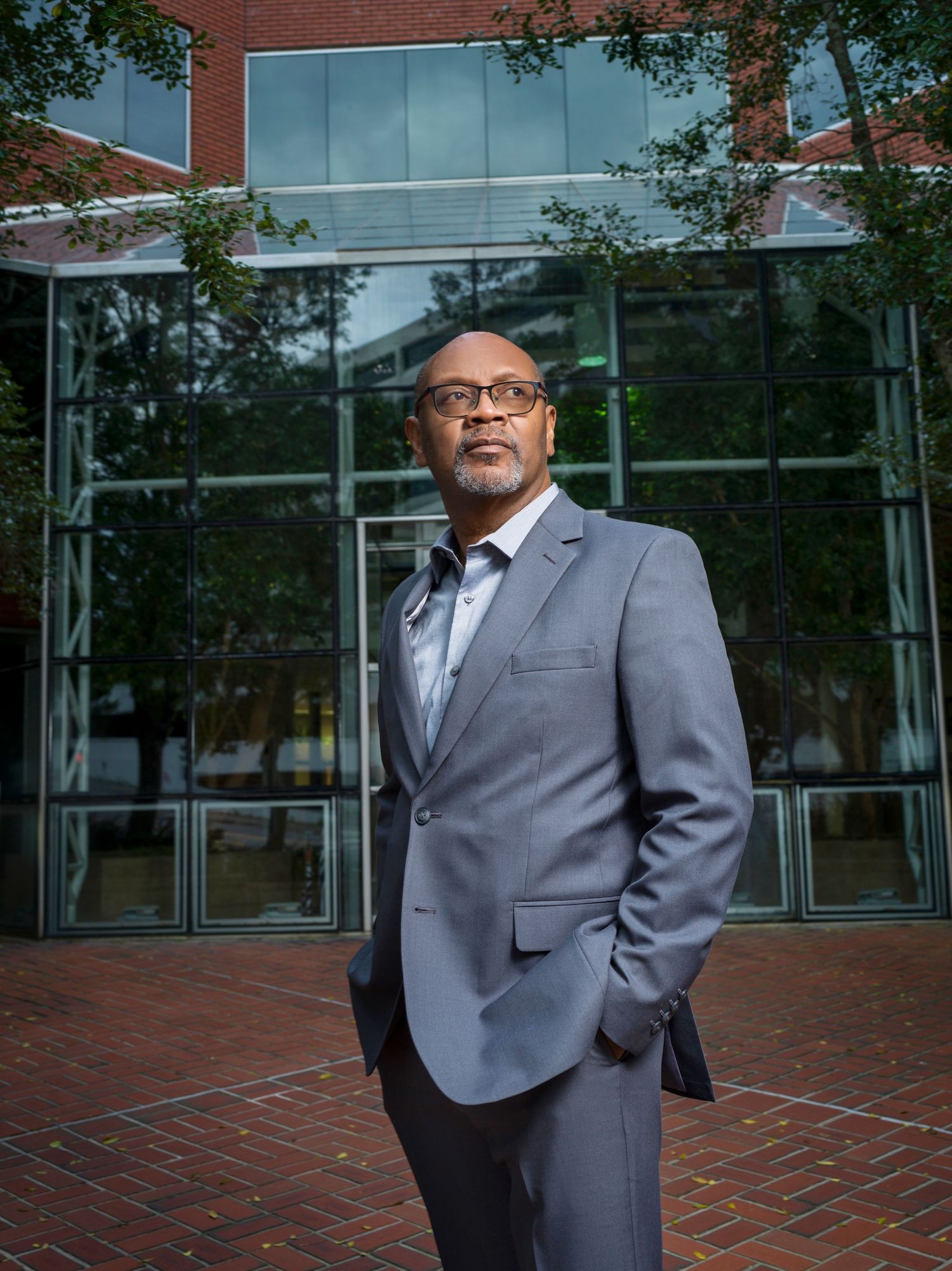 Professional headshots of person in gray suit jacket standing outside modern office building.