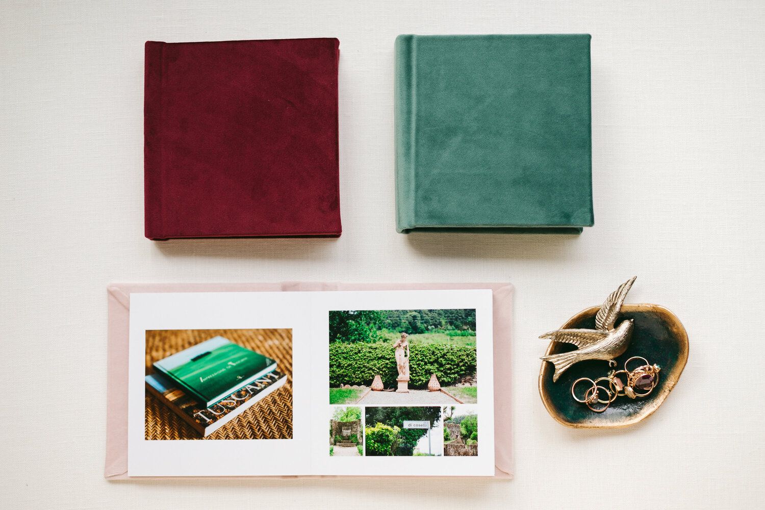Burgundy and green photo albums displayed with wedding photographs on white surface.