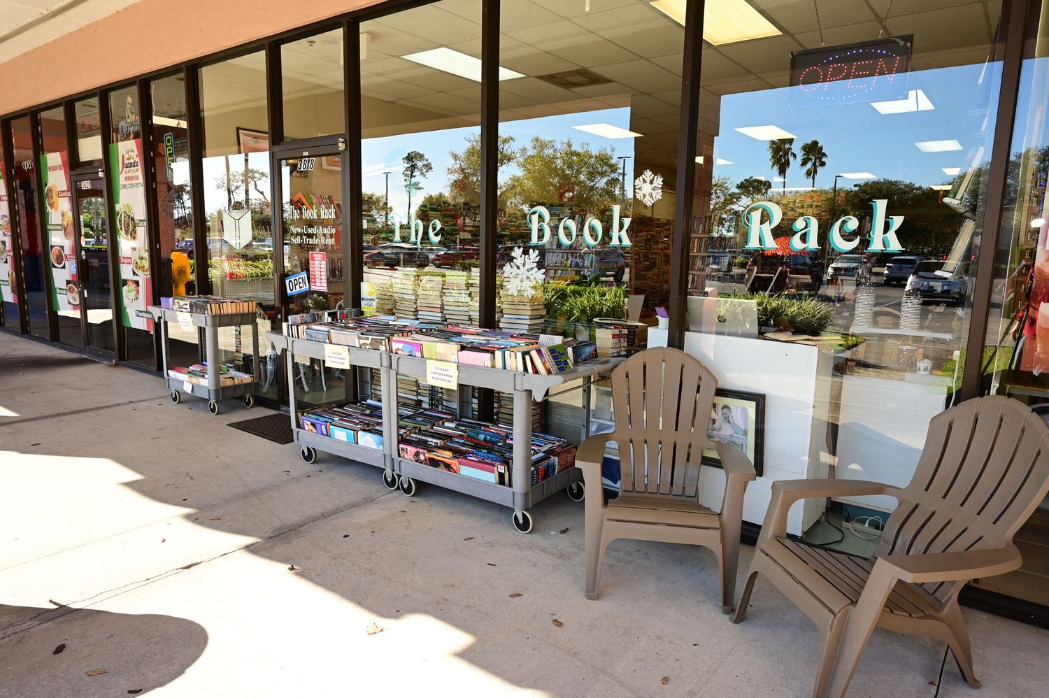 Outdoor view of a bookstore facade with sidewalk displays and palm trees visible in background.
