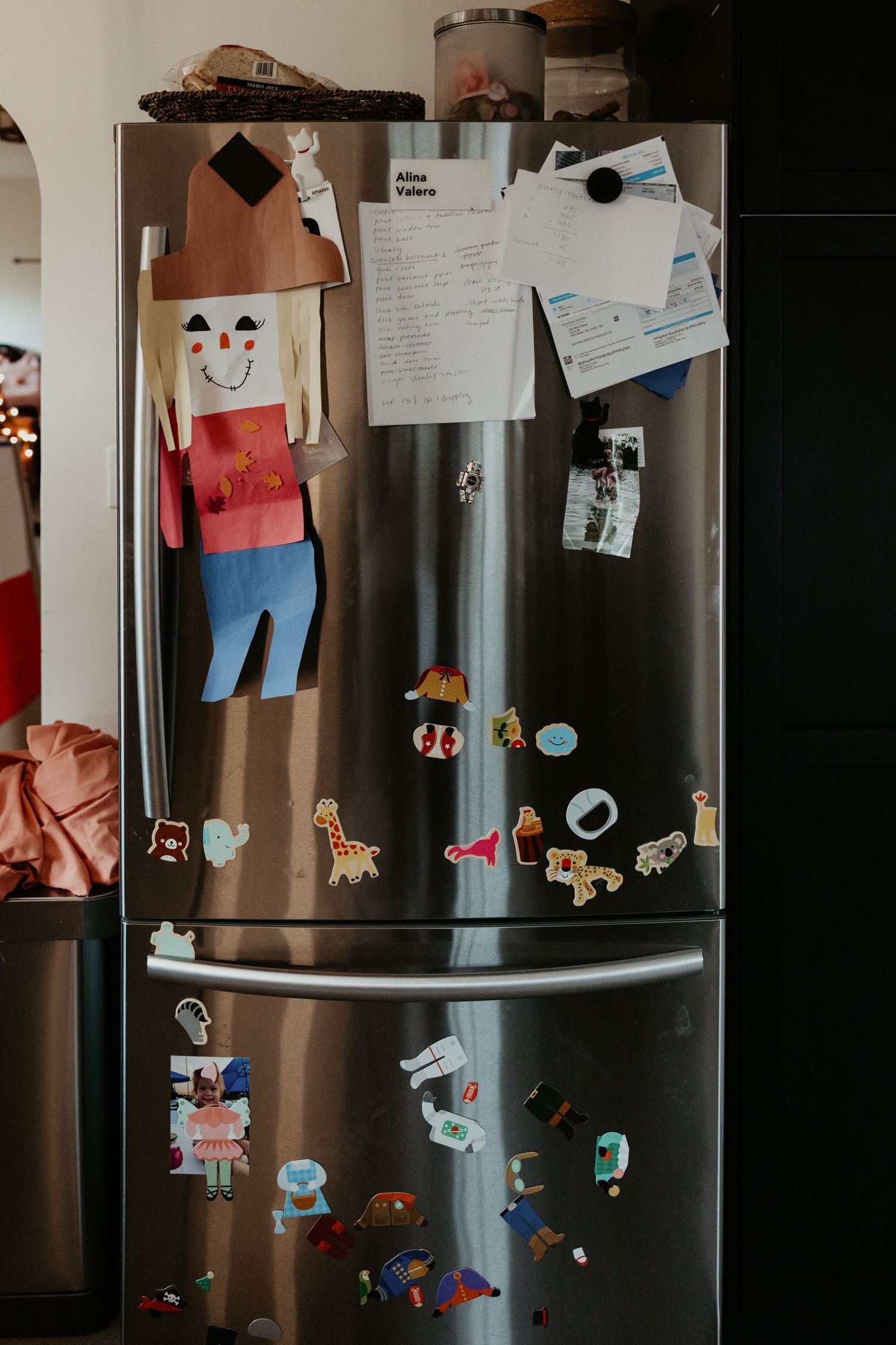 Stainless steel refrigerator covered in colorful magnets and childrens artwork in a home kitchen. Miranda Photo & Co