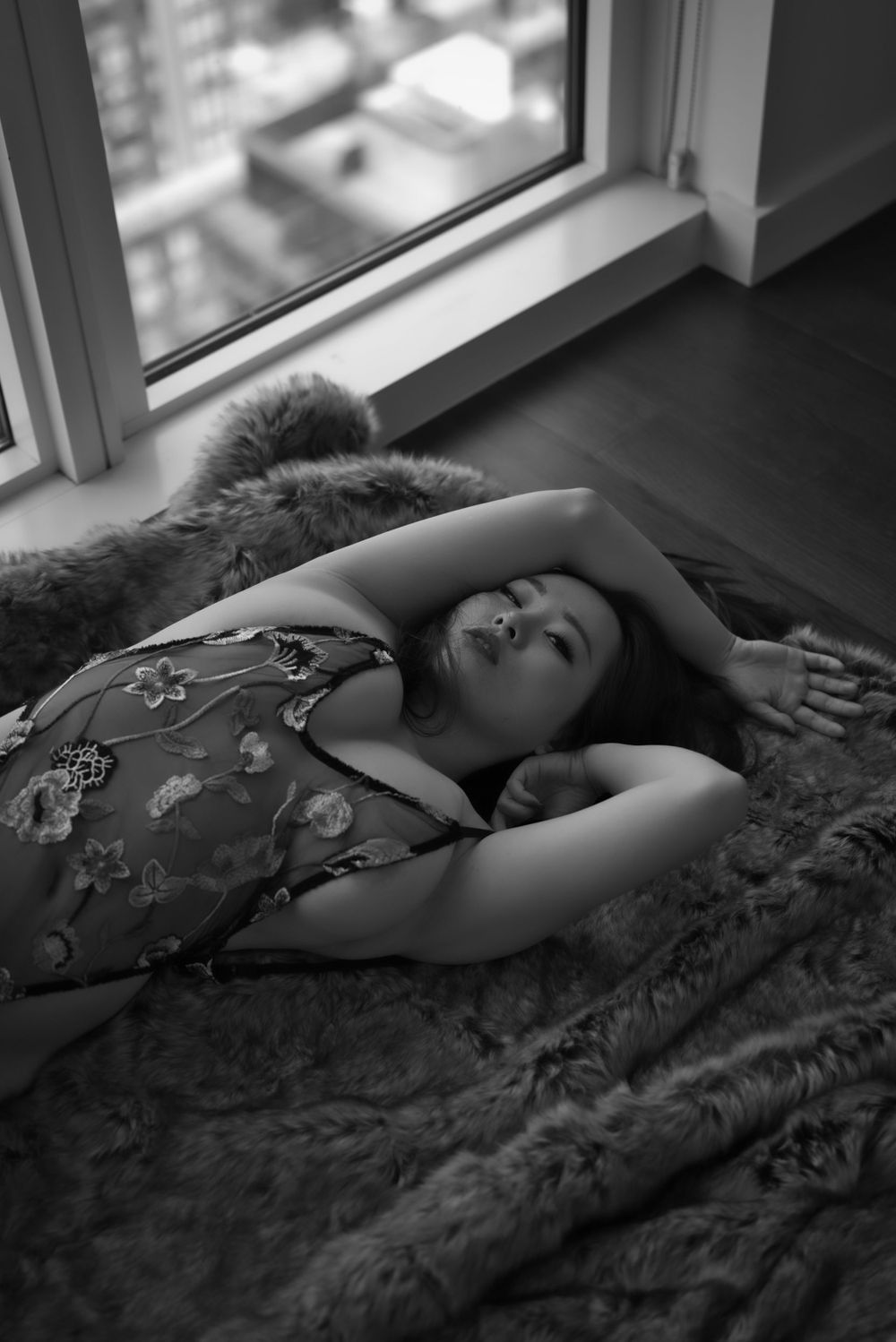Artistic boudoir photo of a person lying on fur blanket near window in patterned lingerie.