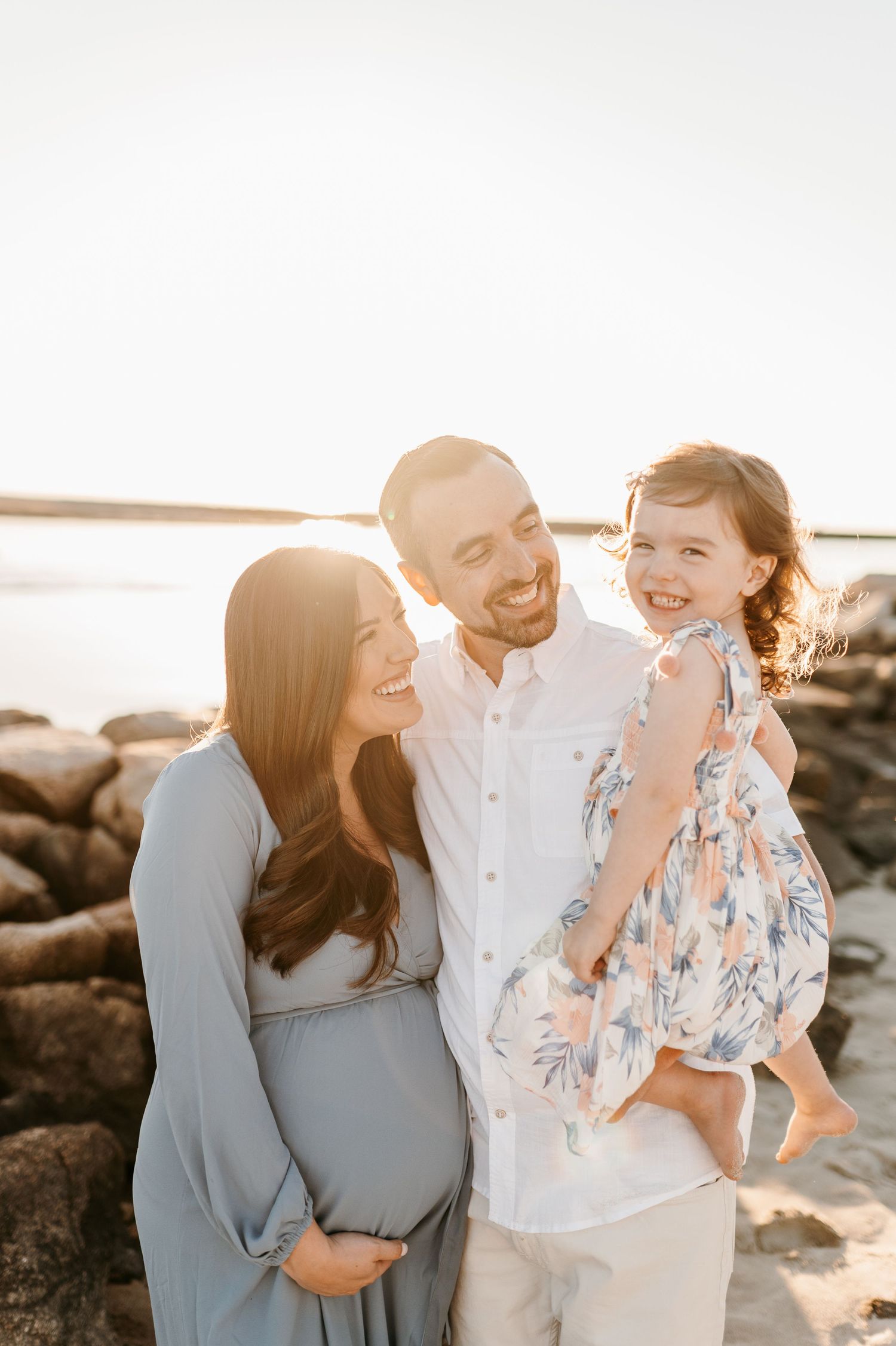 Family laughing together on rocky beach during golden hour photo session.