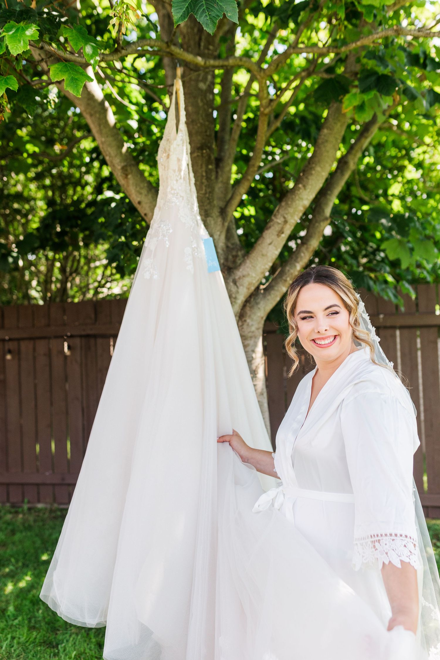 Beautiful white wedding gown displayed outdoors against lush green garden backdrop.