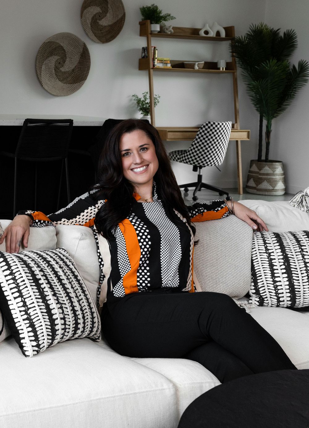 Modern living room featuring white couch with geometric black and orange accent pillows.