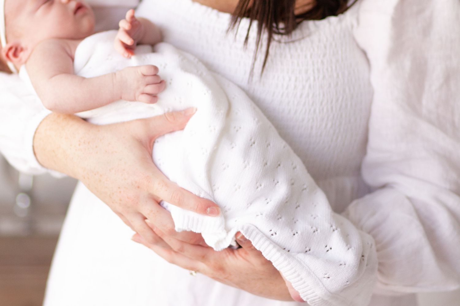 Baby in white blanket being held by mom for her newborn photos.