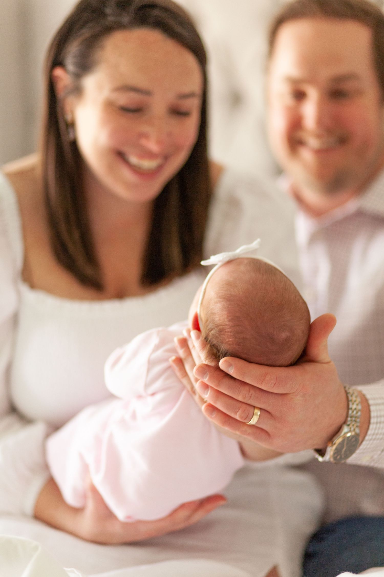 Happy couple gazes lovingly at their newborn baby while sitting together in soft natural light.