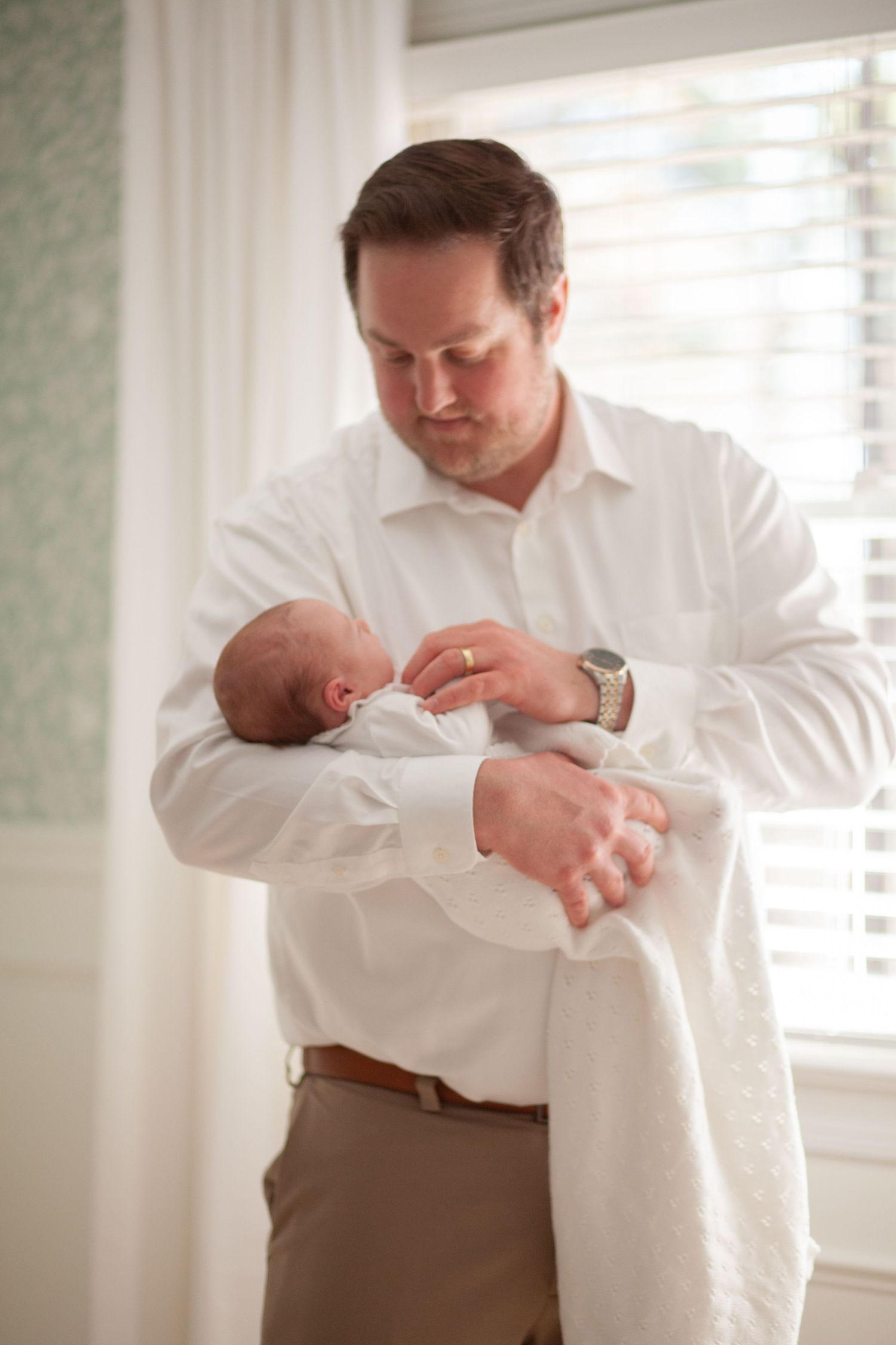 A tender moment between father and newborn baby as they bond near a sunlit window.