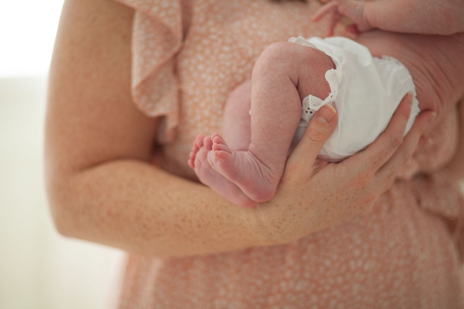 A tiny newborn baby's foot rests in someone's gentle hands while wearing a white cloth diaper.