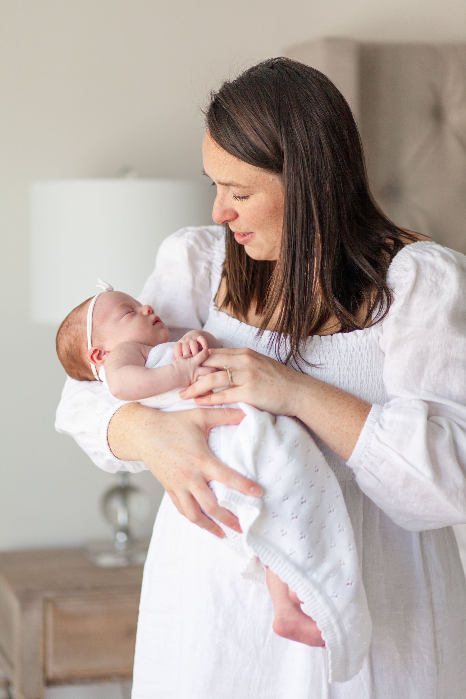A tender moment as a woman in a white dress cradles and gazes lovingly at a newborn baby wrapped in white.