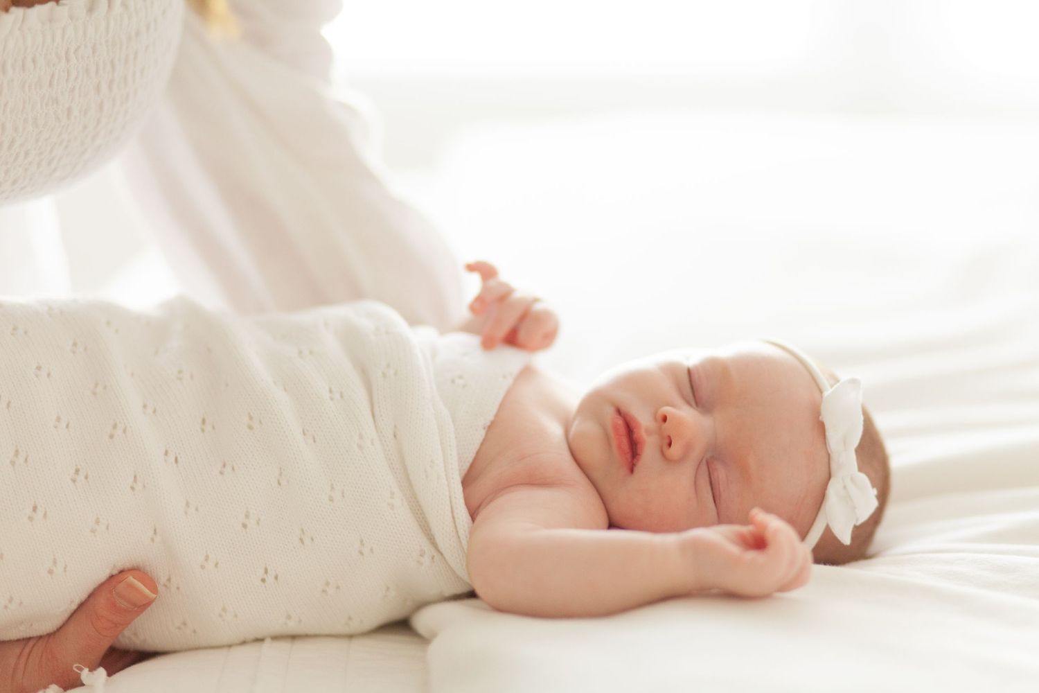 Peaceful newborn baby sleeping soundly on white bedding while wearing a soft cream-colored outfit.