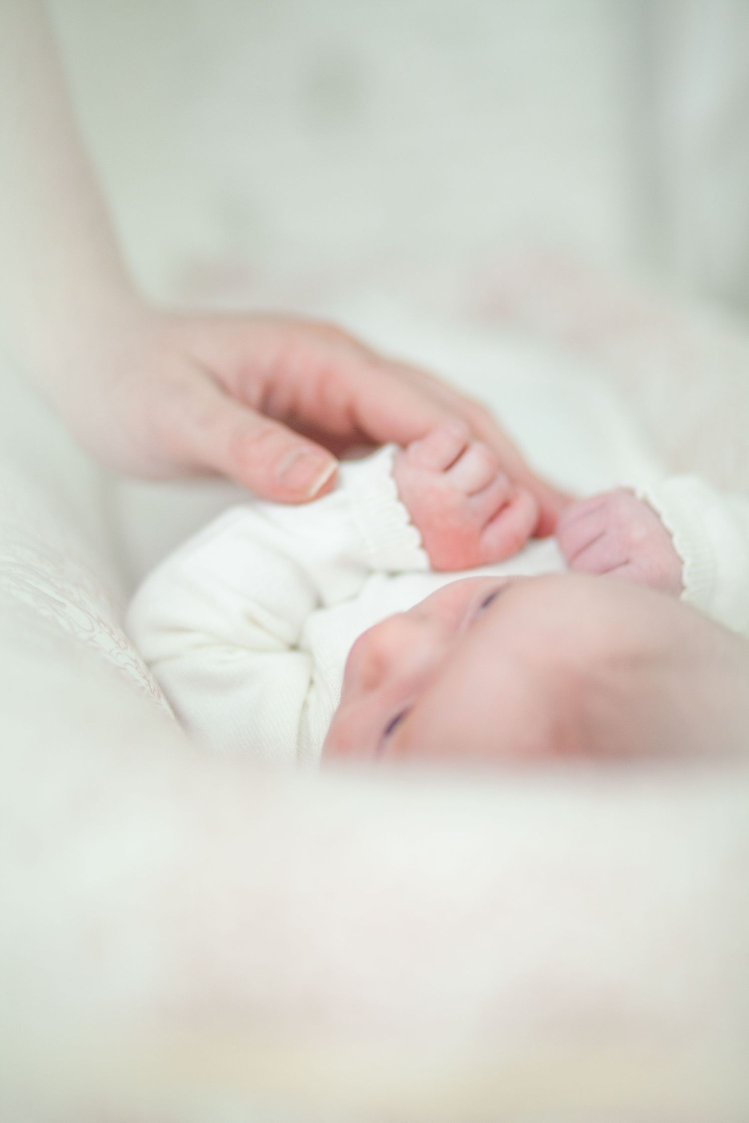 Close up view of a sleeping newborn baby's tiny hand resting on soft white fabric.