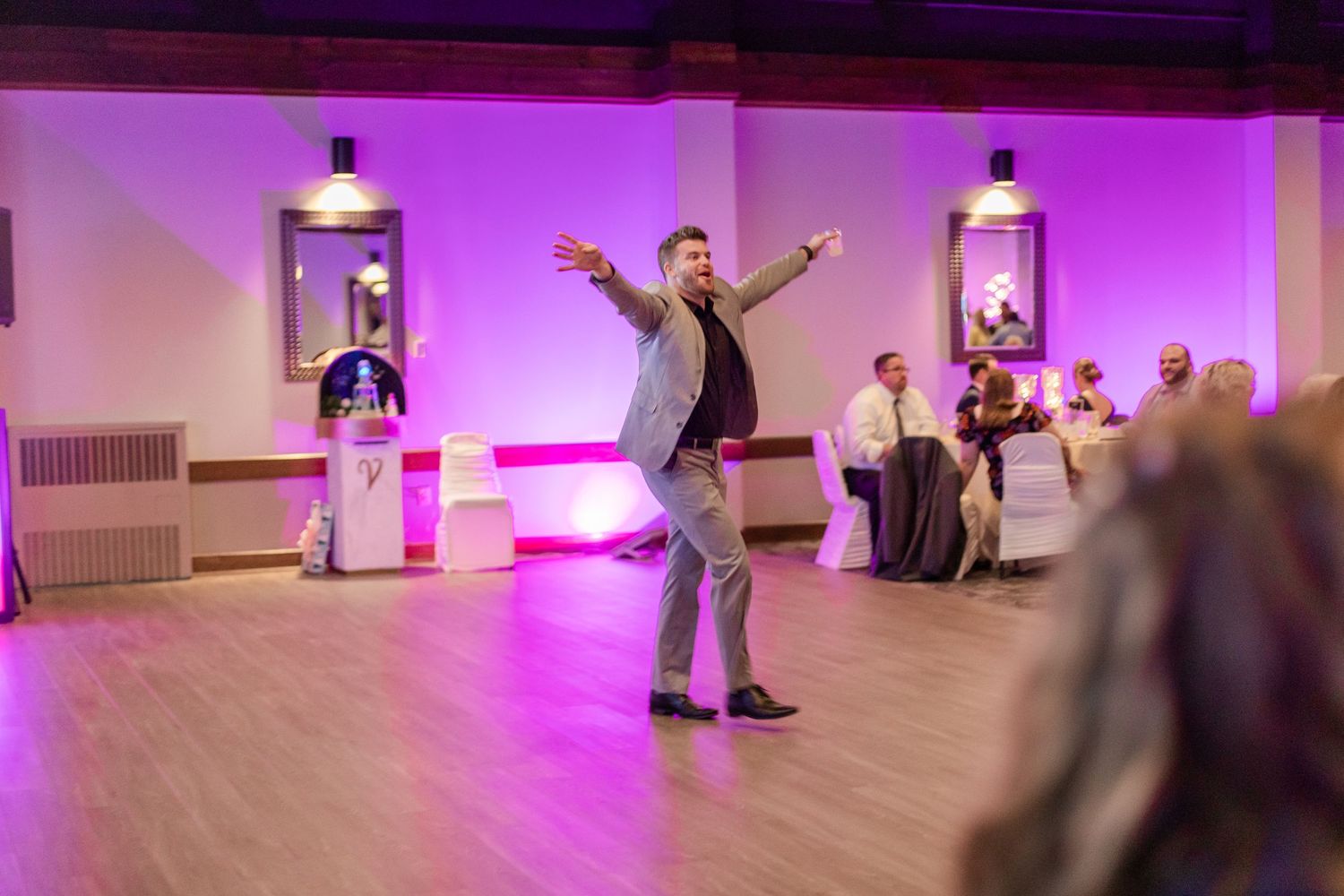 A guest dances enthusiastically on the wooden dance floor at a wedding reception.