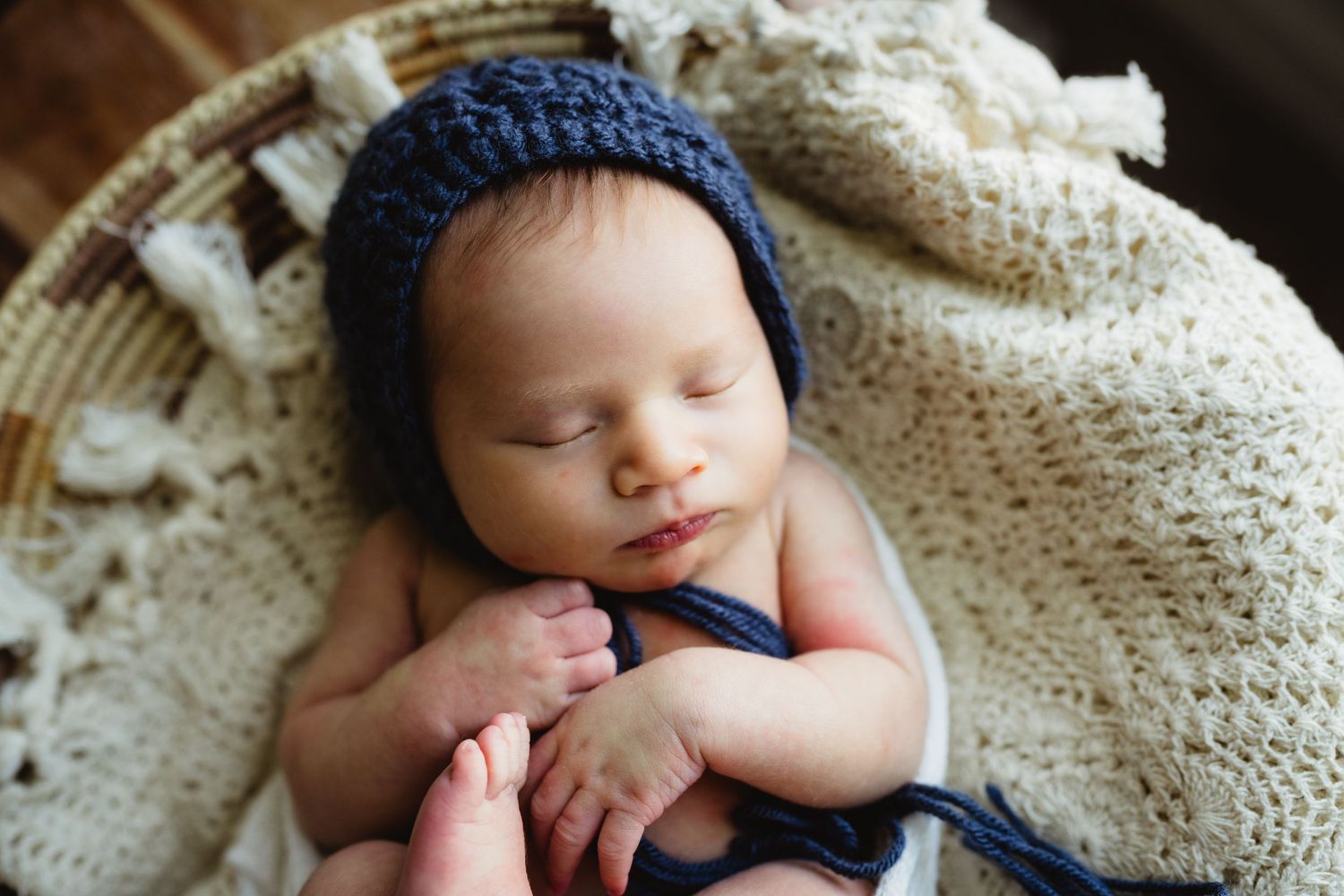 Sleeping newborn in navy blue hat rests peacefully on cream knit blanket.