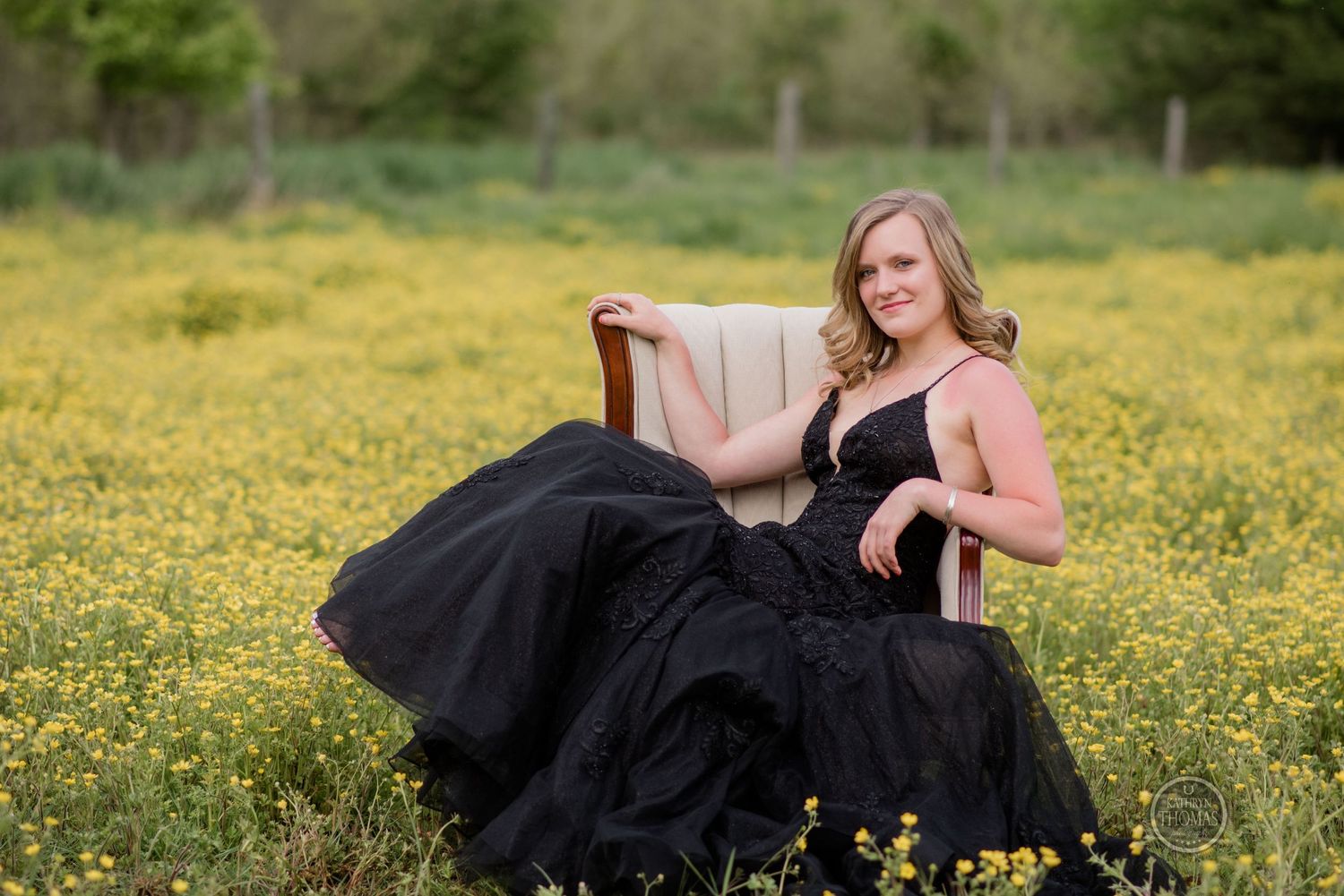 A figure wearing a flowing black dress reclines in a beige chair in a meadow filled with yellow flowers.