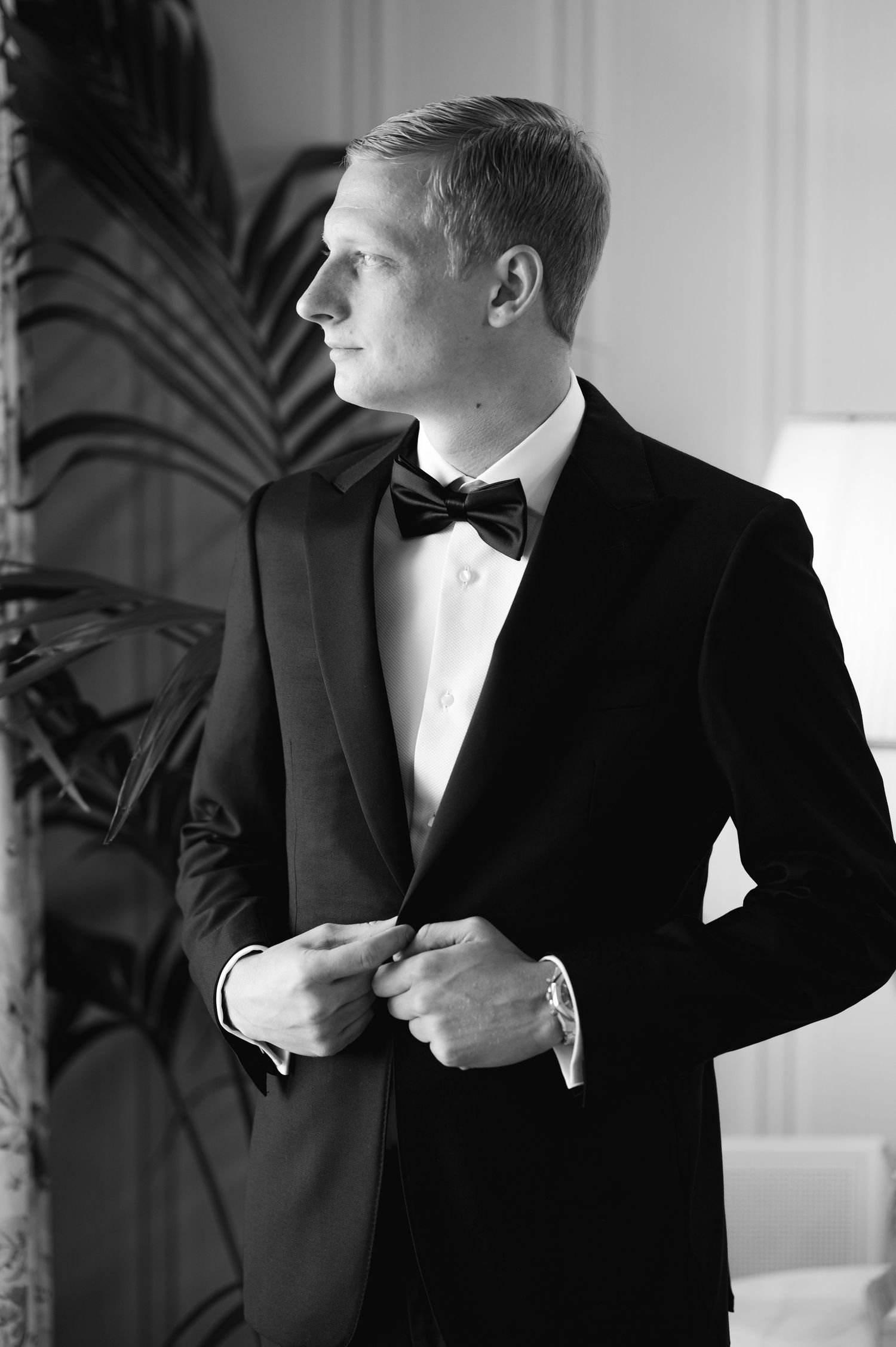 A formal portrait in black and white of someone adjusting their tuxedo.