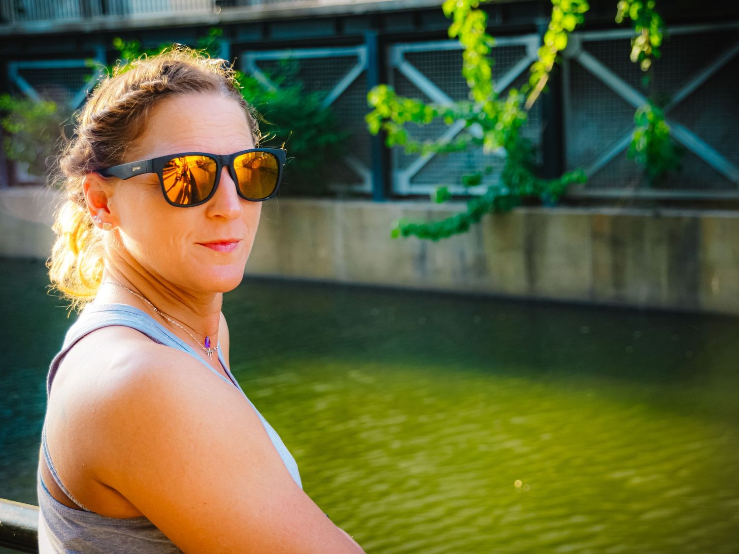 Summer portrait by green water with sunglasses reflecting bright sunlight.