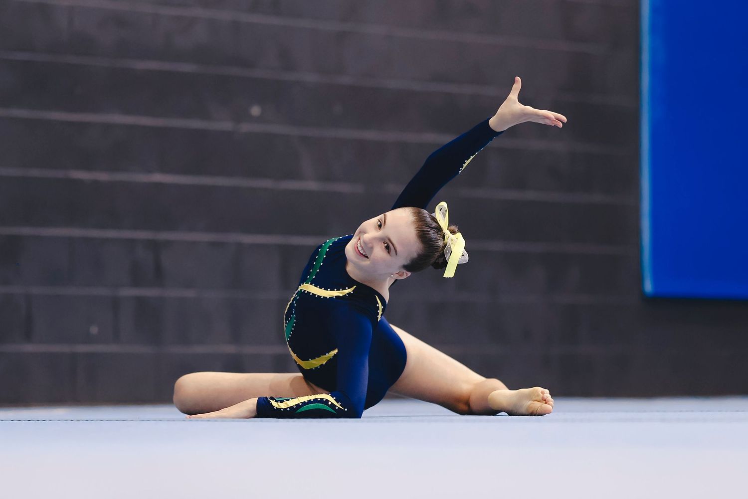 Gymnast in dark leotard performs graceful floor routine with arm extended.