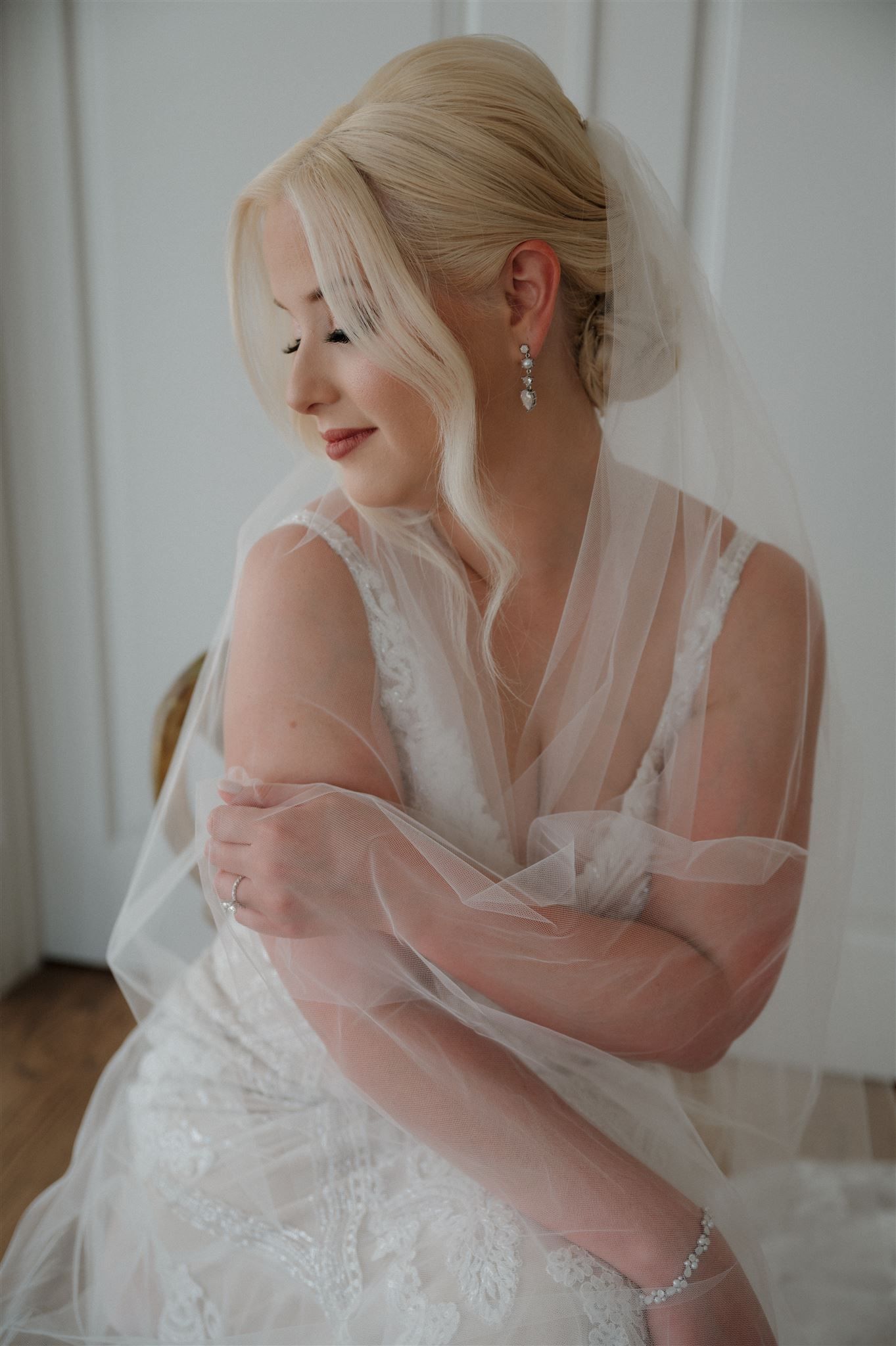 Intimate portrait of a bride wrapped in tulle veil wearing delicate crystal earrings.