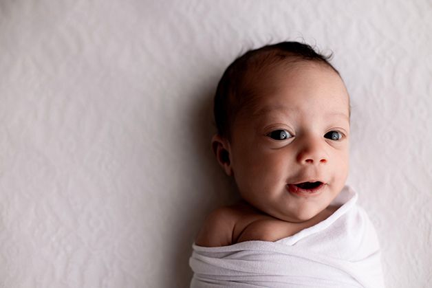 Swaddled newborn baby smiling against white background.