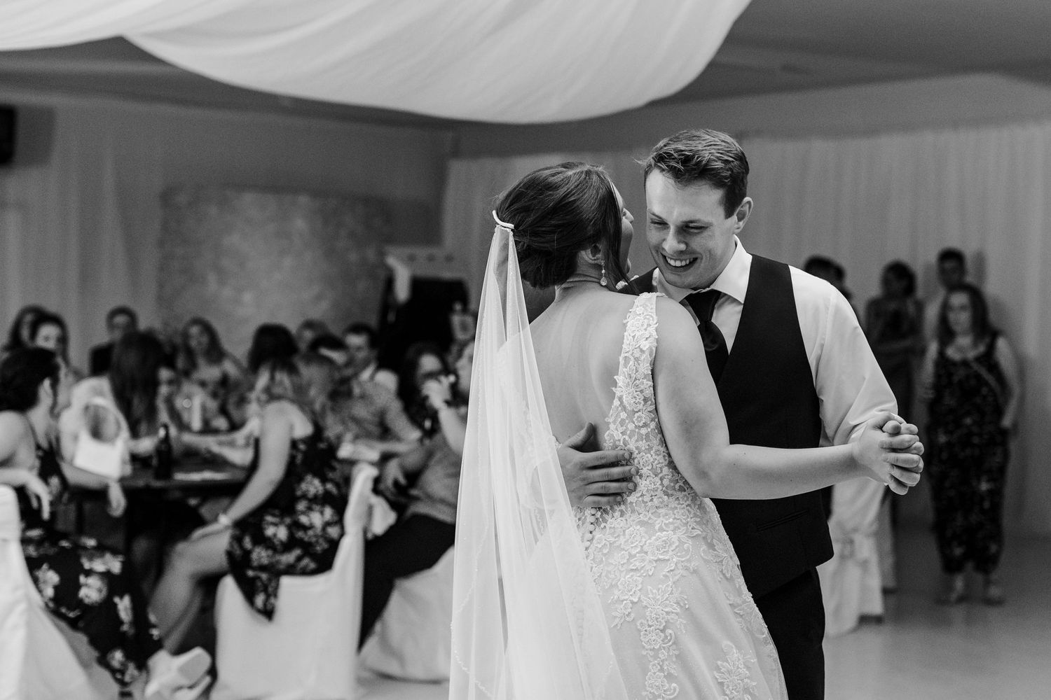 A wedding couple shares their first dance in a white tent with guests watching.
