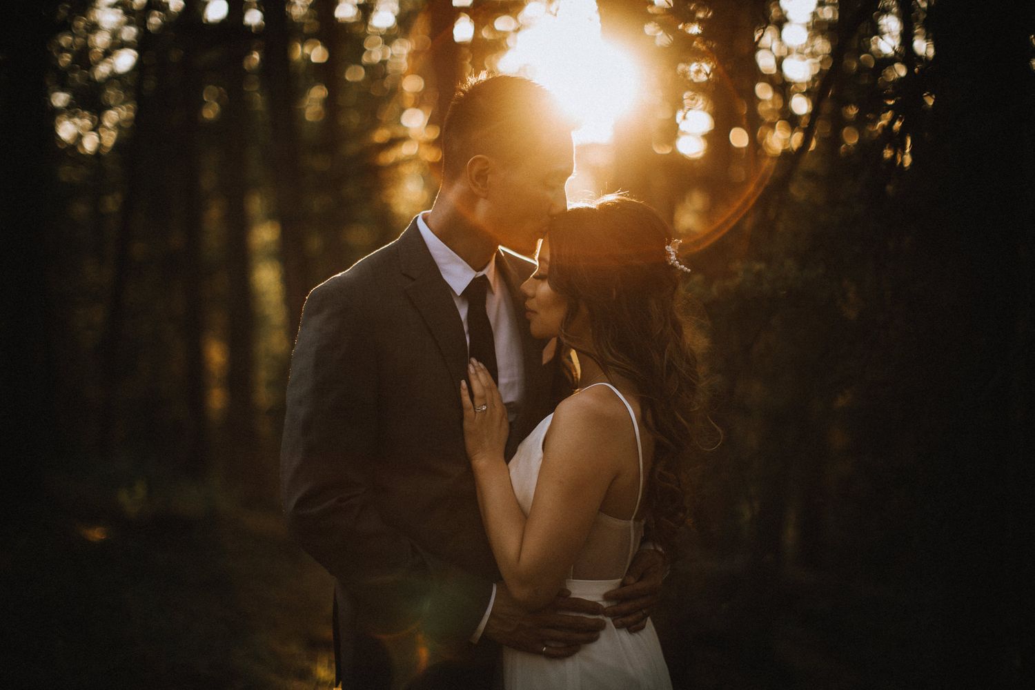A sunset wedding photo in a forest with golden light streaming through the trees.