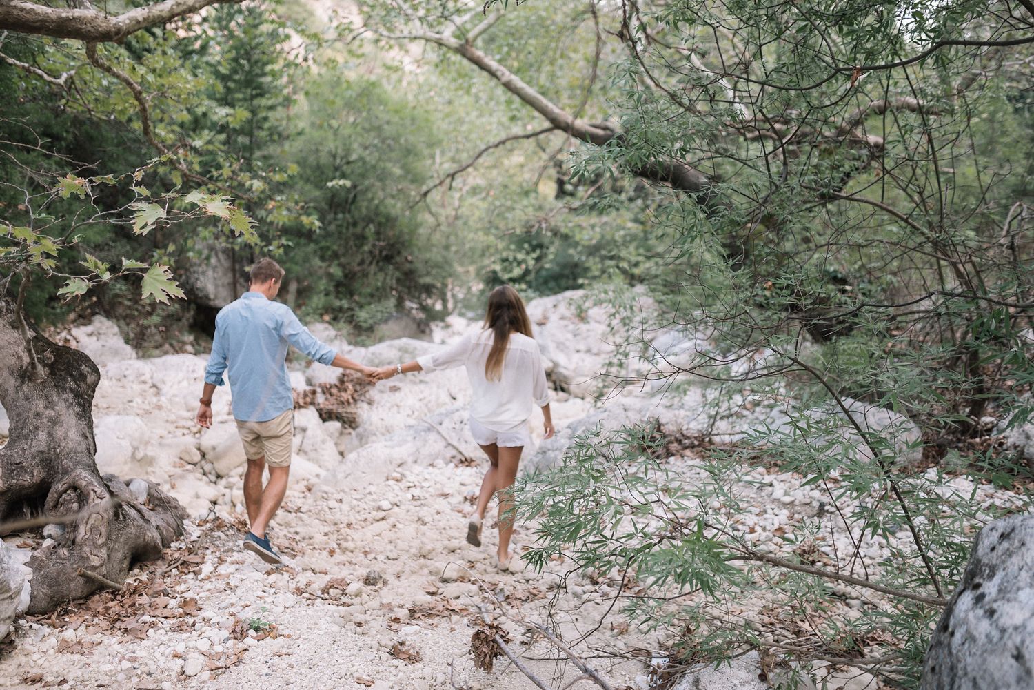 A carefree couple running hand in hand along a rocky natural path surrounded by trees.