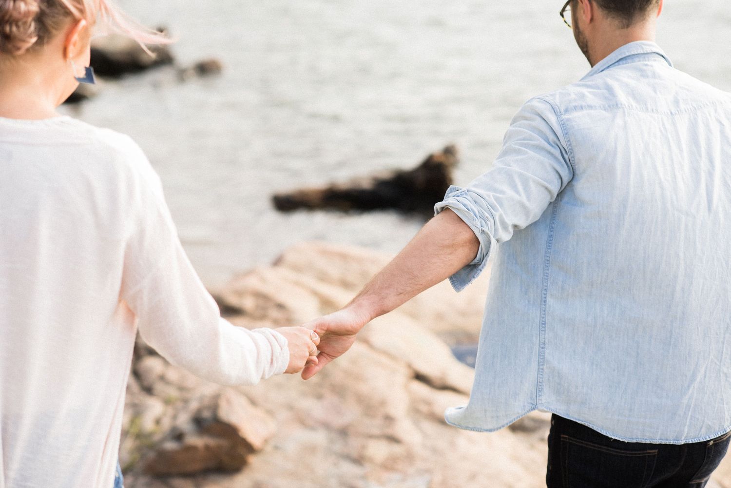 A couple holding hands while walking along a rocky beach in soft lighting.