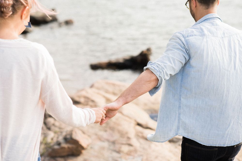 A couple holding hands while walking along a rocky beach in soft lighting.