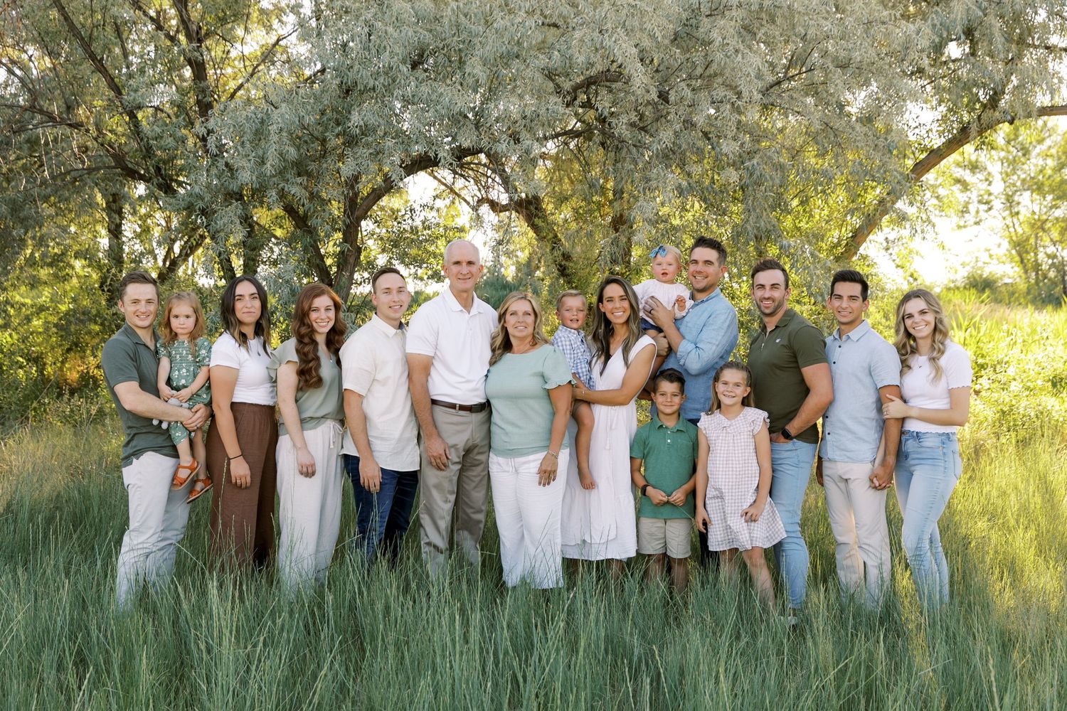 Extended family poses together in coordinated outfits under blossoming trees at sunset.